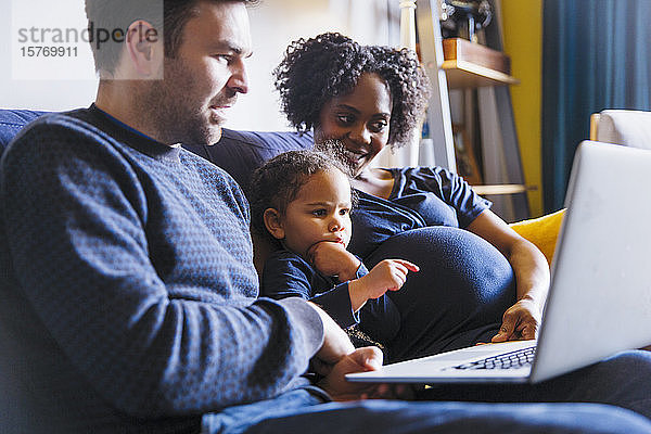 Junge schwangere Familie mit Laptop auf dem Sofa