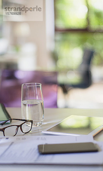 Wasserglas und Brille auf Tisch mit Papierkram