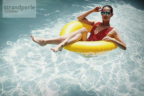 Porträt selbstbewusste Frau entspannt  schwimmt in aufblasbaren Ring in sonnigen Sommer Schwimmbad