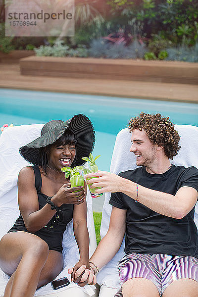 Glückliches junges multiethnisches Paar trinkt Cocktails am Pool