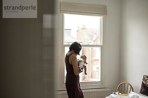 Mutter hält unschuldigen neugeborenen Jungen am Fenster