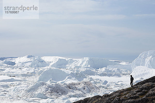 Mann steht auf einer Klippe mit Blick auf die Gletschereisschmelze in Grönland
