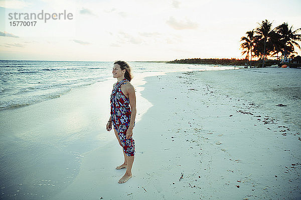 Unbeschwerte Frau im Sonnenkleid am ruhigen Meeresstrand in Mexiko