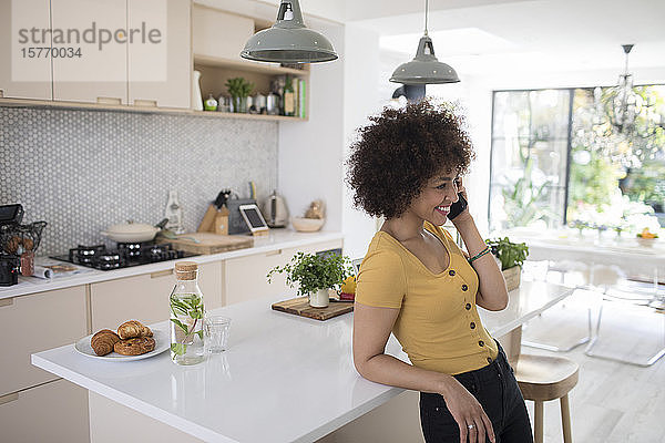 Lächelnde junge Frau  die in der Küche mit ihrem Smartphone telefoniert