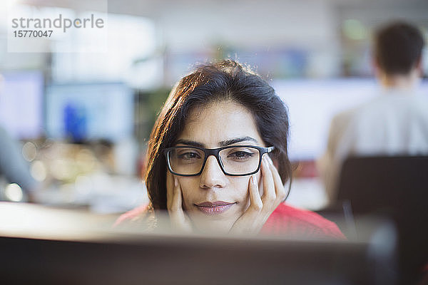 Konzentrierte Geschäftsfrau mit dem Kopf in den Händen  die im Büro am Computer arbeitet