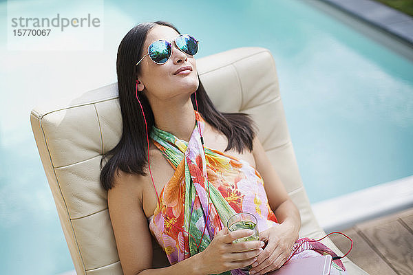Gelassene Frau mit Sonnenbrille und Kopfhörern beim Entspannen und Musikhören am Sommerpool