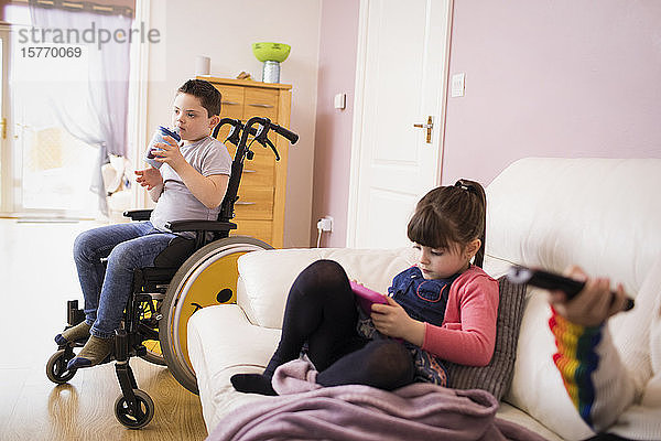 Junge mit Down-Syndrom im Rollstuhl und Schwester im Wohnzimmer
