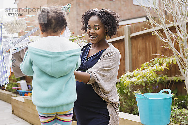 Glückliche schwangere Mutter und Tochter hängen Wäsche auf die Wäscheleine