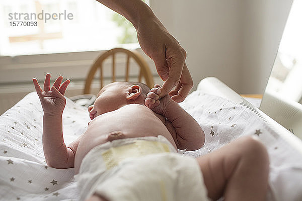 Mutter hält Hände mit neugeborenem Baby Sohn auf Wickeltisch liegend