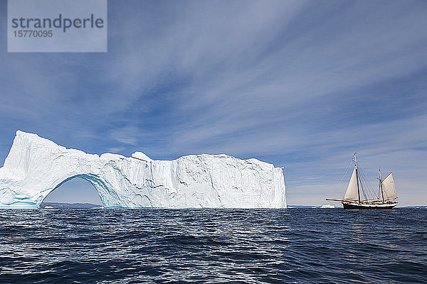 Schiff fährt auf sonnigen majestätischen Eisberg mit Bogen Grönland