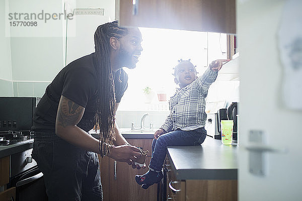 Glücklicher Vater Sohn setzt Schuhe auf Kleinkind Sohn in der Küche