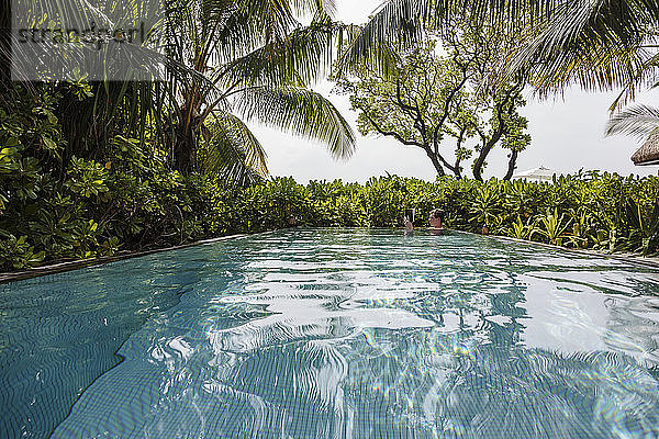 Tropische Palmen umgeben einen Mann  der im Schwimmbad ein Buch liest  Malediven