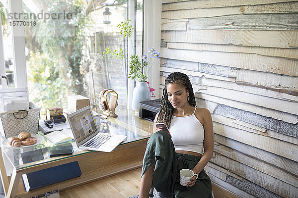 Junge Frau mit Kaffee und Smartphone im Heimbüro