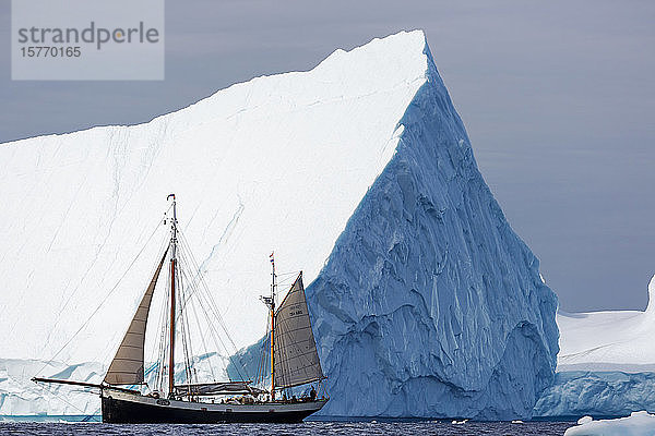 Schiff fährt unter majestätischem Eisberg Atlantik Grönland