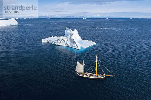 Schiff fährt an Eisberg vorbei auf sonnigem blauen Atlantik Grönland