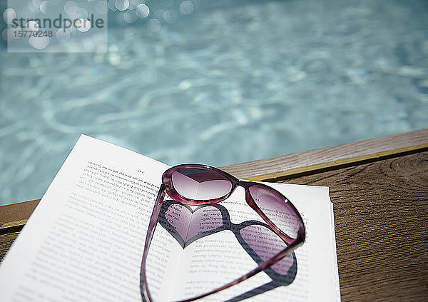 Sonnenbrille in Herzform auf Buch am sonnigen Swimmingpool