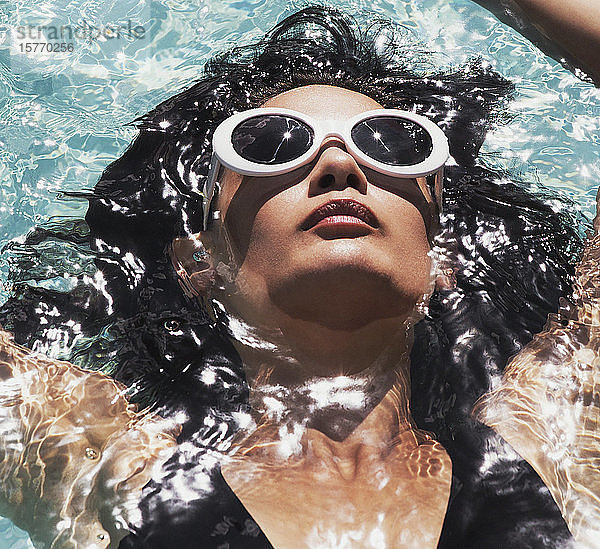 Close up heitere Frau mit Sonnenbrille entspannen  schwimmen in sonnigen Sommer Schwimmbad