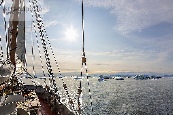 Schiff in der Nähe von schmelzenden Eisbergen auf dem sonnigen  ruhigen Atlantik in Grönland