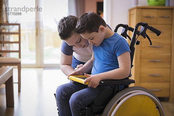 Junge mit Down-Syndrom benutzt digitales Tablet im Rollstuhl