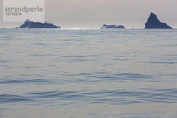 Eisberge in der Ferne auf dem sonnigen  ruhigen  blauen Atlantischen Ozean Grönlands