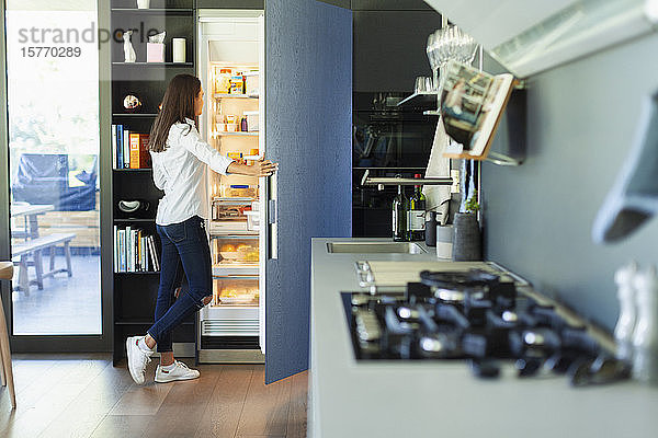 Frau steht am offenen Kühlschrank in der Küche