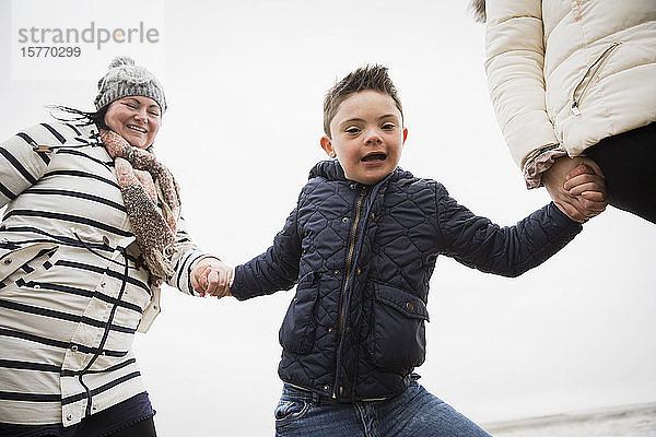 Porträt eines glücklichen  unbekümmerten Jungen mit Down-Syndrom  der mit seiner Mutter Händchen hält