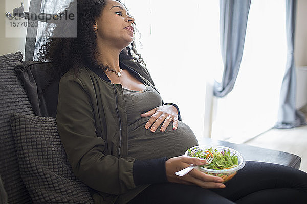 Müde junge schwangere Frau isst Salat