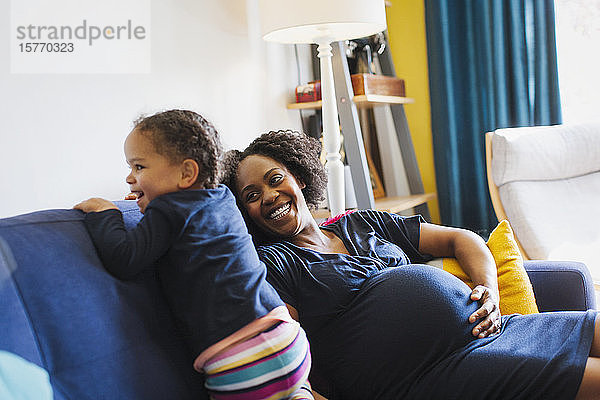 Verspielte schwangere Mutter und Tochter auf dem Sofa