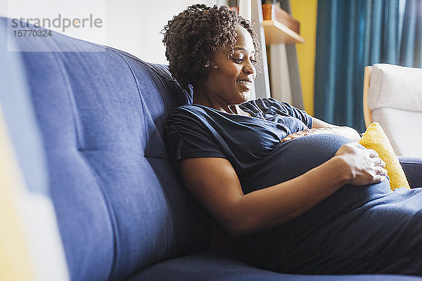 Glückliche schwangere Frau berührt Bauch auf Sofa