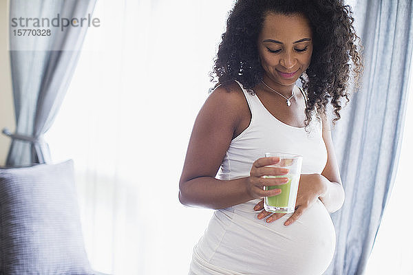 Junge schwangere Frau trinkt grünen Smoothie