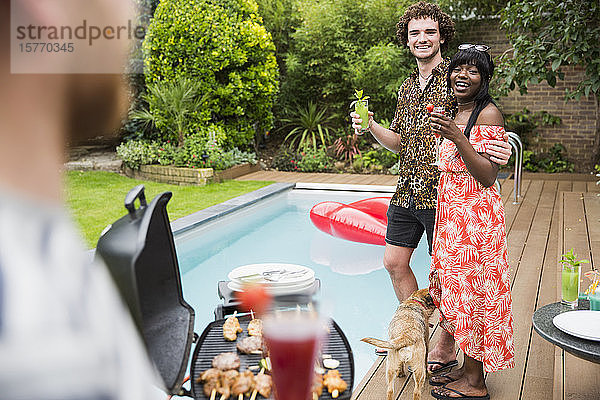 Glückliches junges Paar genießt Cocktails und grillt am Swimmingpool