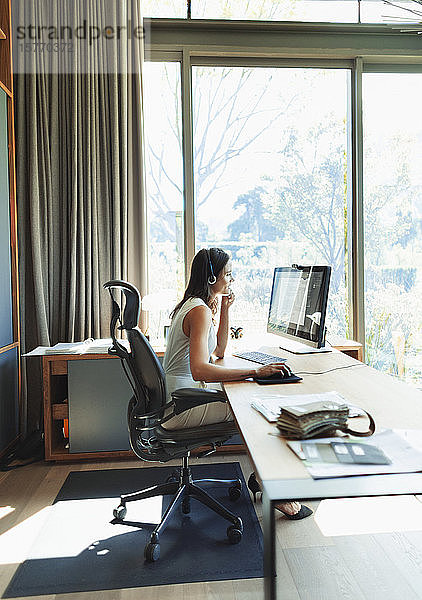Geschäftsfrau mit Headset bei der Arbeit am Computer im Heimbüro