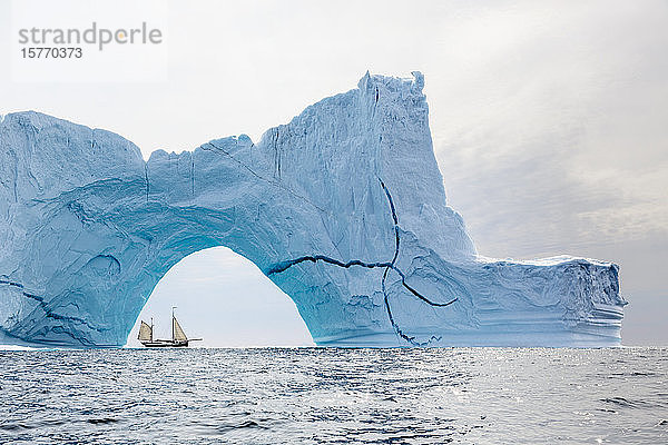 Schiff fährt hinter einem majestätischen Eisbergbogen auf dem Atlantik Grönland