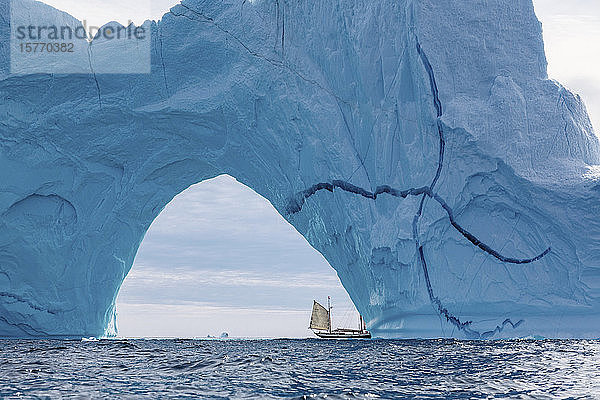 Segelboot unter majestätischem Eisbergbogen Atlantik Grönland