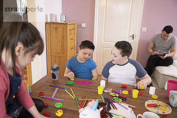 Junge mit Down-Syndrom und Geschwister spielen mit Spielzeug am Tisch