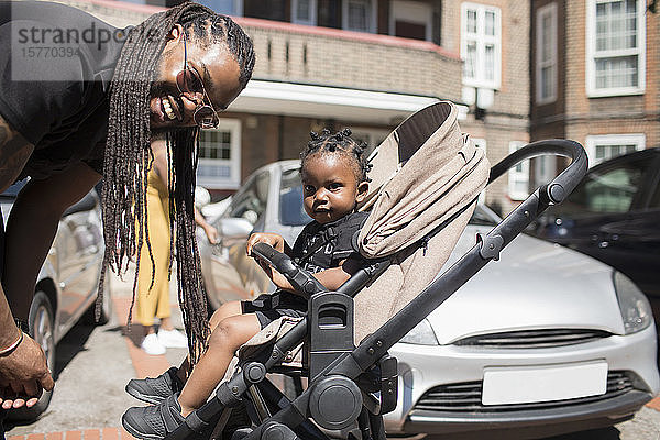 Porträt glücklicher Vater mit langen Zöpfen und Kleinkind Sohn im Kinderwagen auf sonniger Straße