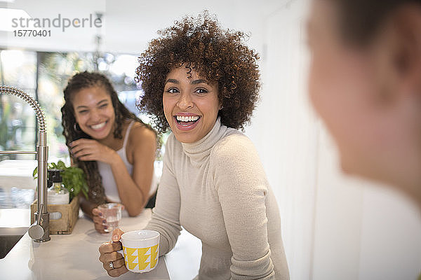 Glückliche junge Frauen Freunde lachen und trinken Tee in der Küche