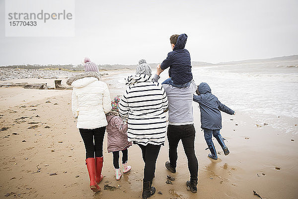 Familie in warmer Kleidung beim Spaziergang am winterlichen Meeresstrand