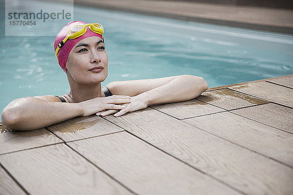 Selbstbewusste Frau mit Badekappe und Schwimmbrille lehnt sich an den Rand des Schwimmbeckens