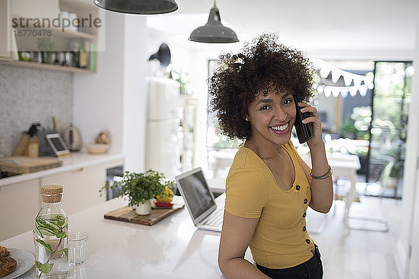 Porträt einer glücklichen jungen Frau  die in der Küche mit einem Smartphone telefoniert