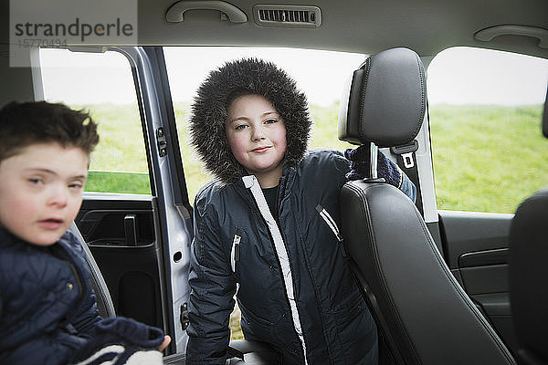 Porträt selbstbewusster Junge in Pelzkapuzenjacke auf dem Rücksitz eines Lieferwagens