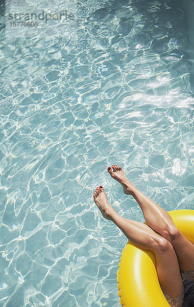 Frau mit nackten Füßen  die in einem aufblasbaren Ring im sonnigen Schwimmbad schwimmt