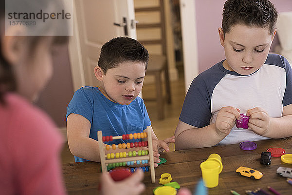Junge mit Down-Syndrom und Bruder spielen mit Spielzeug am Tisch