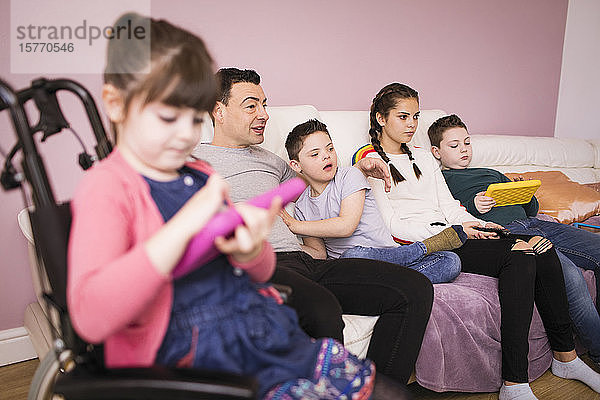 Familie mit Kind mit Down-Syndrom sieht auf dem Wohnzimmersofa fern
