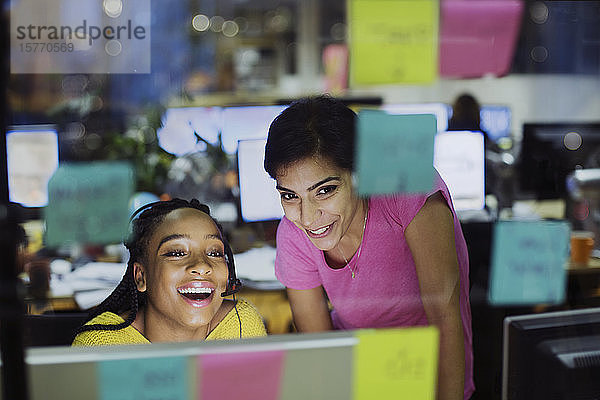 Glückliche Geschäftsfrauen mit Computer hinter Haftnotizen im Büro