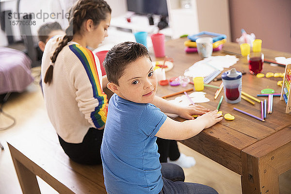 Porträt niedlichen Jungen mit Down-Syndrom Färbung am Tisch mit Schwester