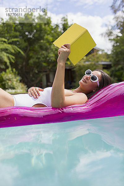 Frau entspannt sich  liest ein Buch auf einem aufblasbaren Floß im Sommerschwimmbad