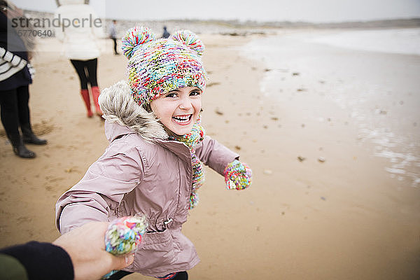 Porträt glückliches sorgloses Mädchen in warmer Kleidung läuft am Winterstrand