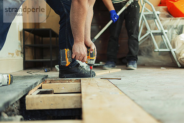 Bauarbeiter mit Bohrmaschine beim Verlegen von Dielen auf einer Baustelle