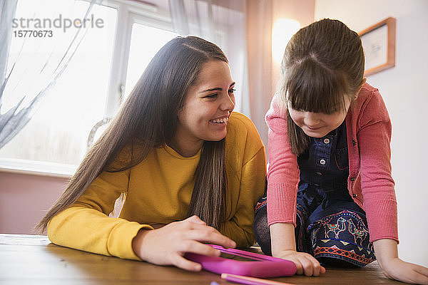 Fröhliche Schwestern mit digitalem Tablet am Tisch